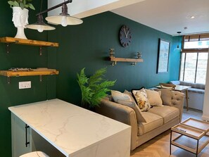 Une cuisine moderne avec un plan de travail en marbre, un mur vert, un canapé et un coin repas offrant une vue sur l’extérieur grâce à une fenêtre.