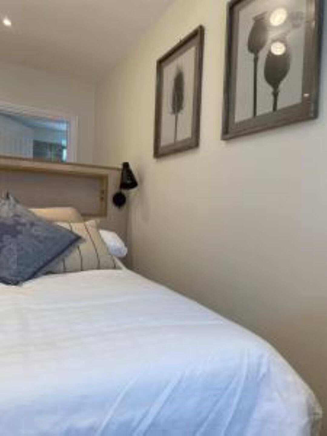 A neatly made bed with a white duvet and a blue pillow, a bedside lamp, and two framed pictures on the wall.