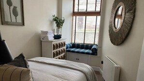 Un dormitorio con cama, un asiento junto a la ventana, un radiador y un espejo en la pared.