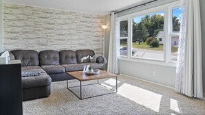 A living room with a sectional sofa, a coffee table, and a large window with curtains.
