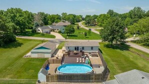 A residential property with a backyard swimming pool, a fenced deck, and a house with a sloped roof.
