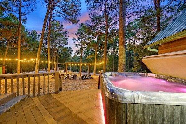 A hot tub with a wooden deck, surrounded by trees and string lights.