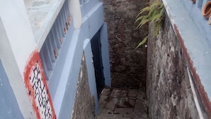 A narrow staircase with stone steps leading to a lower level, flanked by walls with blue and white painted sections and terracotta pots. - HOTEL EL PANECILLO (Quito)