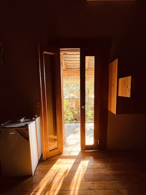 A narrow hallway with wooden flooring leading to a door with a view of greenery outside. - Urbano's Pacific Jungle Hostel (Hicaco)