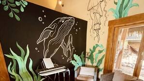 Een gezellig zithoek met rieten meubels, een laptop op een tafeltje en een muurschildering van een walvis.