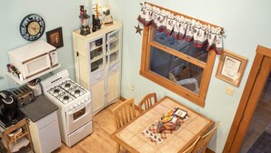 A compact kitchen with a gas stove, microwave, and small refrigerator. There is a dining table with chairs and a window with curtains.