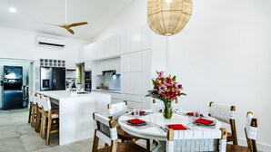 A modern kitchen with white cabinetry, a central island, and a dining area with a round table and chairs. - Newly Renovated, Beachfront, 3 bed Condo on Exclusive Langosta Beach! (Tamarindo, Guanacaste Province)