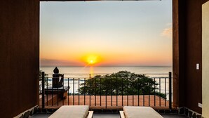 A balcony with two lounge chairs, a view of the sunset over the sea, and a stone wall. - Newly Renovated, Beachfront, 3 bed Condo on Exclusive Langosta Beach! (Tamarindo, Guanacaste Province)