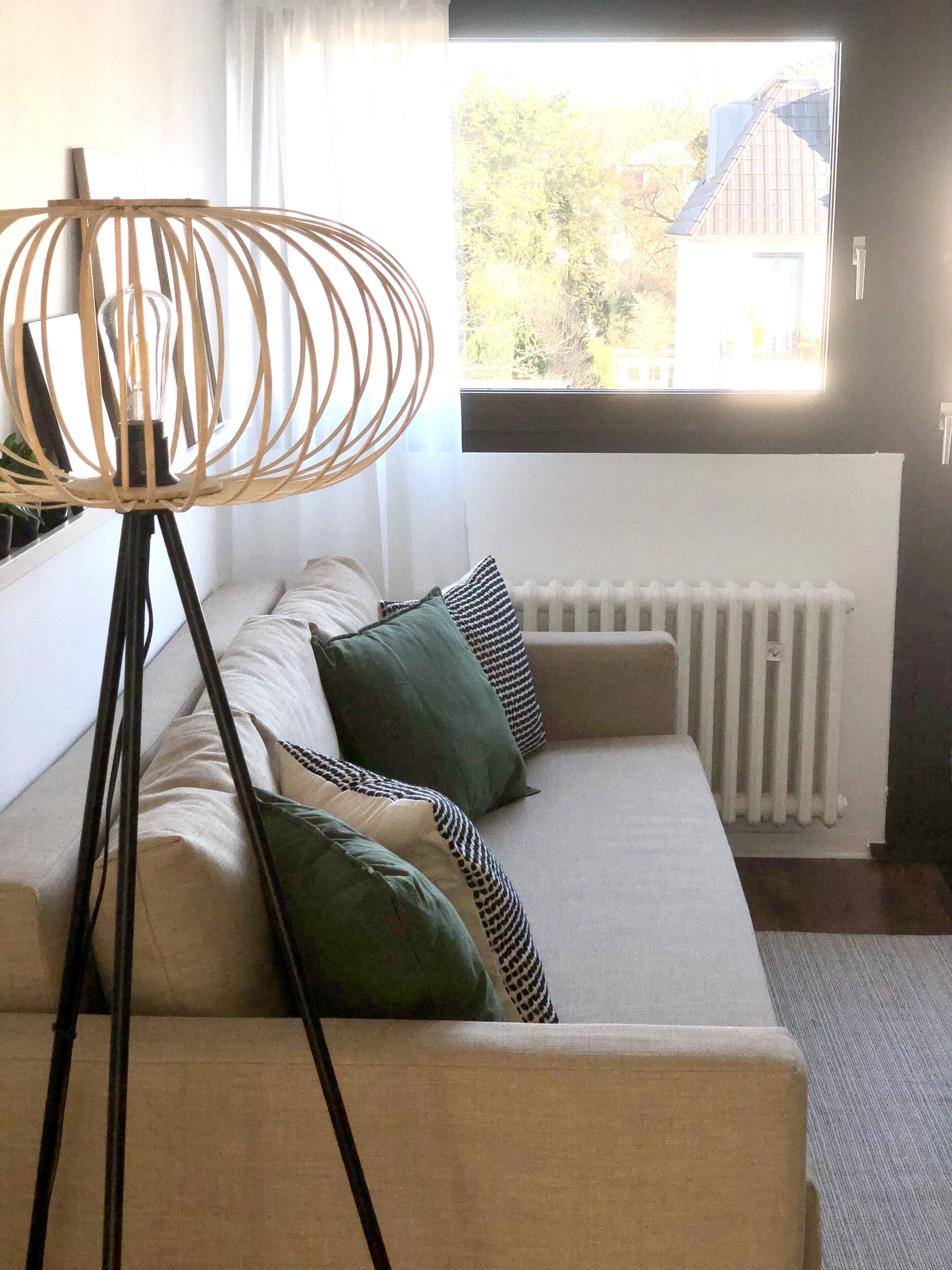 A modern living room with a sectional sofa, a unique woven floor lamp, and a view of the outside through a large window.