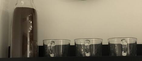 A kitchen with a black clock, a glass pitcher, and three clear cups on a black shelf.