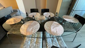 Un espace repas moderne avec une table en verre entourée de chaises, d’un canapé et d’un élément décoratif mural.