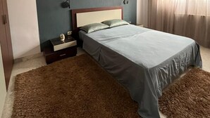 Une chambre à coucher avec un lit, des tables de chevet, une commode, un lustre et une fenêtre avec des rideaux.