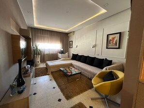 A modern living room with a sofa, a coffee table, a yellow armchair, and a large window with curtains. - Apartment in the Corniche Sousse tourist district (Sousse)