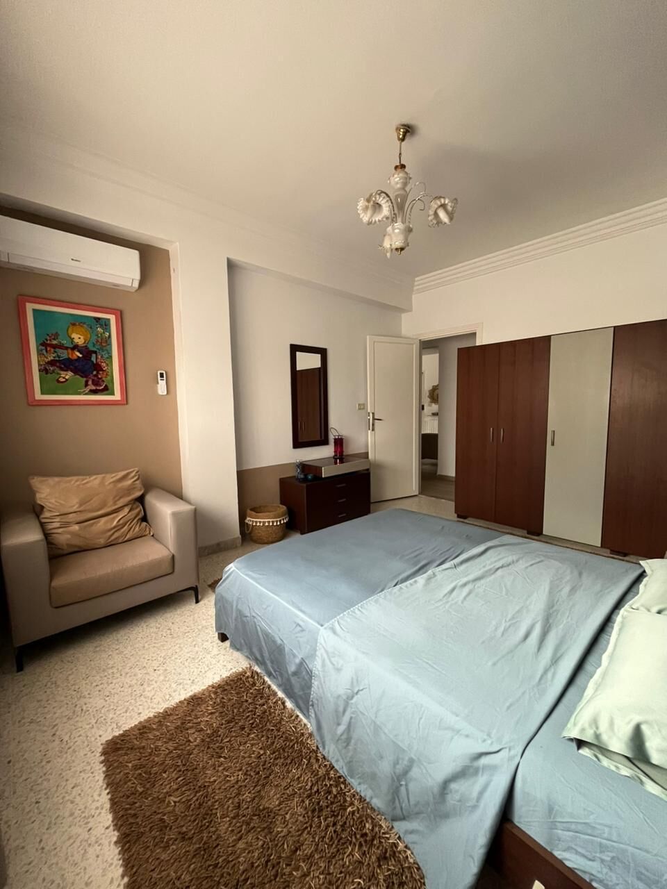 A bedroom with a bed, a sofa, a wardrobe, a mirror, and a ceiling light fixture.