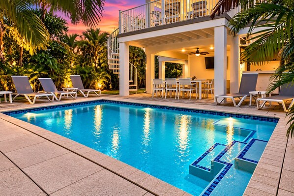 A swimming pool with lounge chairs and a covered seating area, surrounded by palm trees.