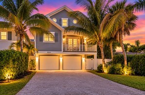 A two-story house with a garage, surrounded by palm trees and a well-maintained lawn.
