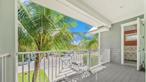 A wooden deck with a white railing, a view of palm trees, and a building entrance. - Prime Holmes Beach Location | Heated Pool | Walk to the Beach (Holmes Beach)