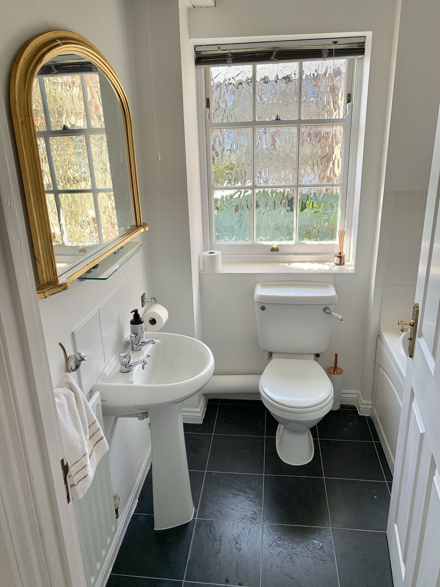 A bathroom with a white sink, toilet, and a window with frosted glass.