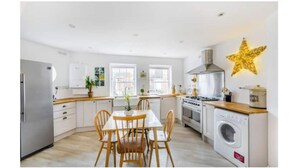A modern kitchen with white cabinetry, a central island with chairs, a stove, and a washing machine. - Historic family house near Longleat (Warminster)