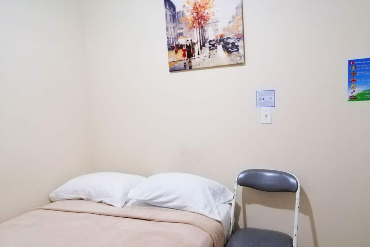 A bedroom with a bed, a chair, and a wall-mounted painting.