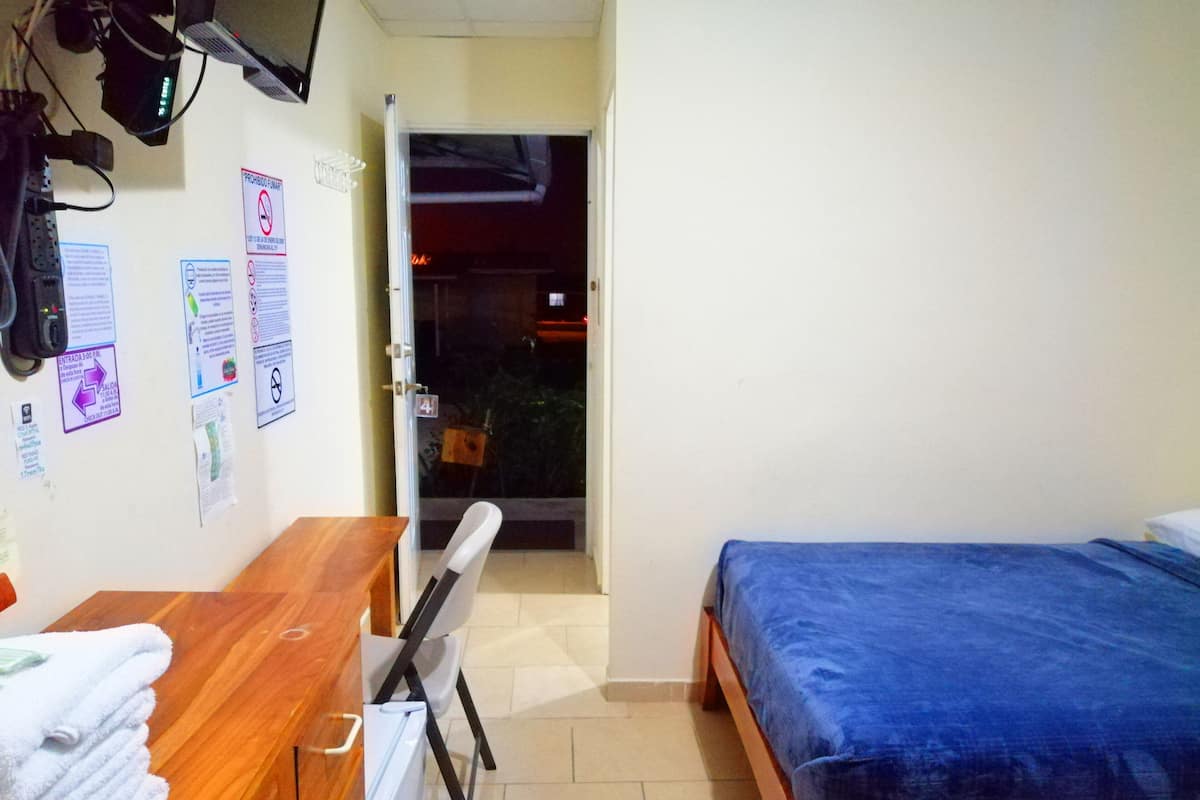 A bedroom with a bed, a desk, a chair, and a television mounted on the wall.