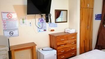 Un dormitorio con un aparador de madera, un refrigerador blanco pequeño, un televisor montado en la pared y una cama.