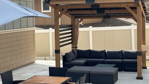 Une terrasse dotée d’une pergola en bois, d’une table à manger avec des chaises et d’un canapé d’extérieur noir.