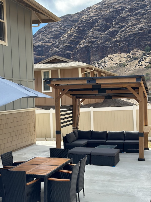 Une terrasse dotée d’une pergola en bois, d’une table à manger avec des chaises et d’un canapé d’extérieur noir.