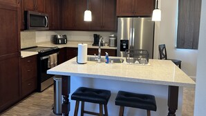 Une cuisine moderne avec des meubles en bois foncé, des appareils en acier inoxydable, un îlot central doté de tabourets et un éclairage suspendu.