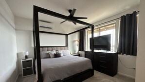 Un lit à baldaquin avec un ventilateur de plafond, une télévision et une table de chevet avec une lampe.