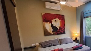 Une chambre à coucher avec un lit, un ventilateur de plafond, un appareil de climatisation, un tableau et une fenêtre.