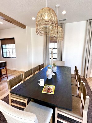 Ein Esszimmer mit einem großen schwarzen Tisch, Holzstühlen und einer gewobenen Leuchte.