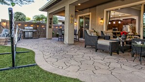 An outdoor patio area with stone flooring, wicker furniture, and a grill.