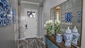 A hallway with a white door, decorative blue and white artwork, a wooden floor, and a blue cabinet with white flowers.