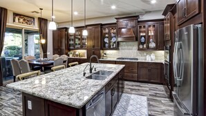 A modern kitchen with dark wood cabinets, granite countertops, stainless steel appliances, and pendant lighting.