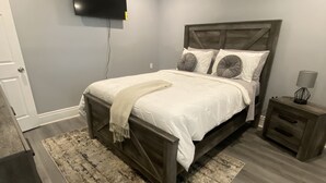 Een slaapkamer met een bed, een aan de muur bevestigde televisie, een nachtkastje en een vloerkleed.