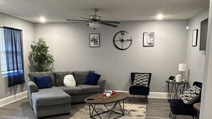 Een moderne woonkamer met een grijze bank, een salontafel, een bijzettafeltje en een plafondventilator.