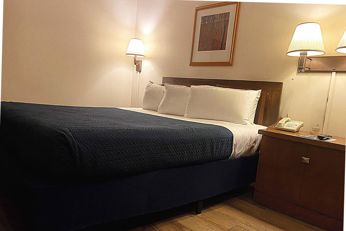 Ein Hotelzimmer mit Bett, Nachttischlampen, einem Telefon und einem kleinen Holzschrank.