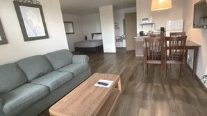 A modern living room with a grey sofa, a wooden coffee table, and a dining area with a wooden table and chairs.