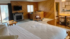 A hotel room with a bed, a fireplace, a television, a sauna, a dining table, and a kitchen area.