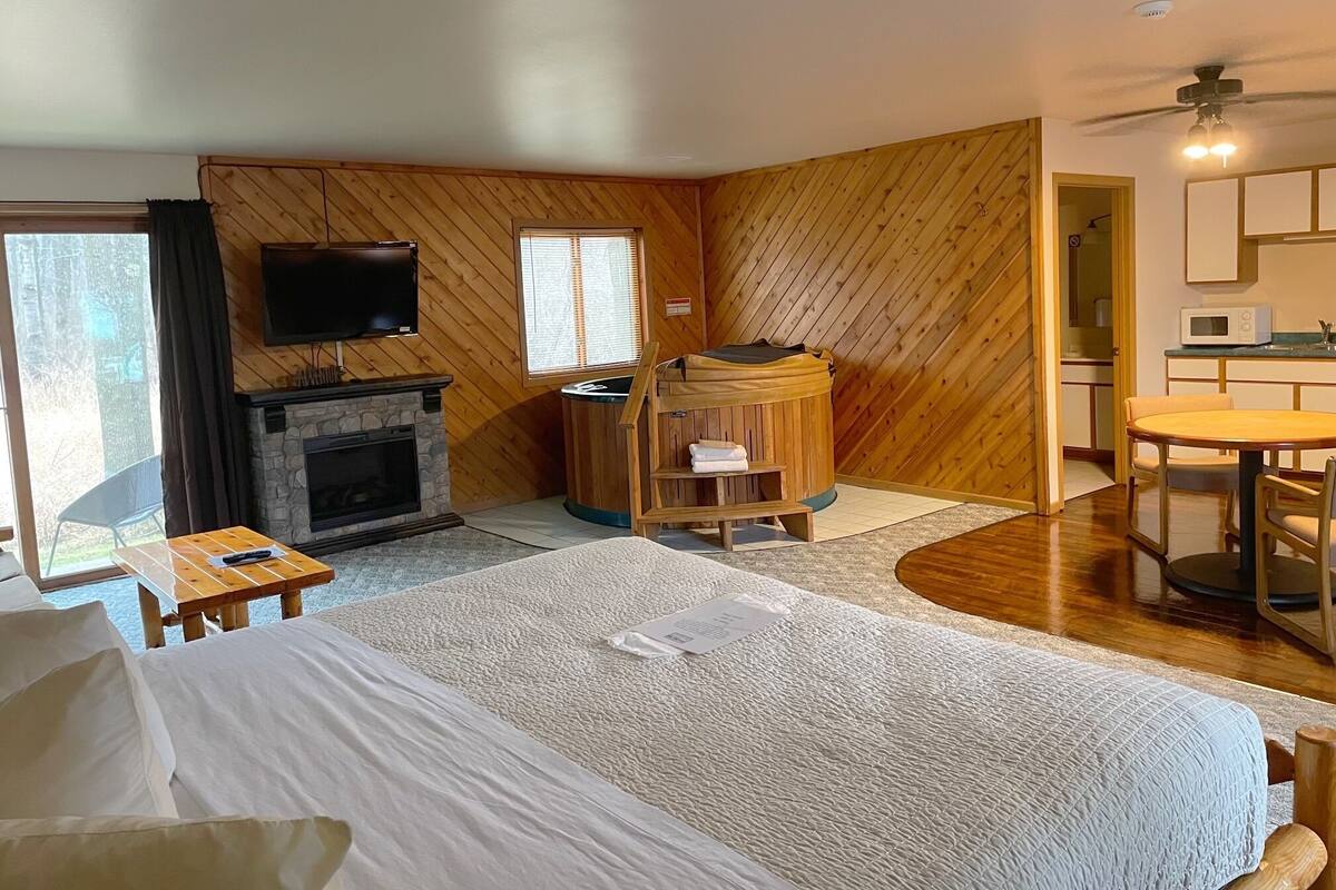Ein Hotelzimmer mit Bett, Kamin, Fernseher, Sauna, Esstisch und Küchenzeile.
