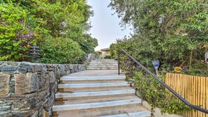 A stone staircase leading to a building, surrounded by lush greenery and a bamboo fence.
