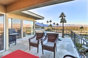 Ein Balkon mit Korbstühlen, einem Grill und Blick auf Palmen und Berge.