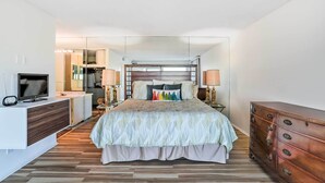 A modern bedroom with a bed, bedside lamps, a dresser, a TV, and a walk-in closet.