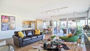 A modern living room with a leather sofa, a glass coffee table, and a dining area with a wooden table and chairs.