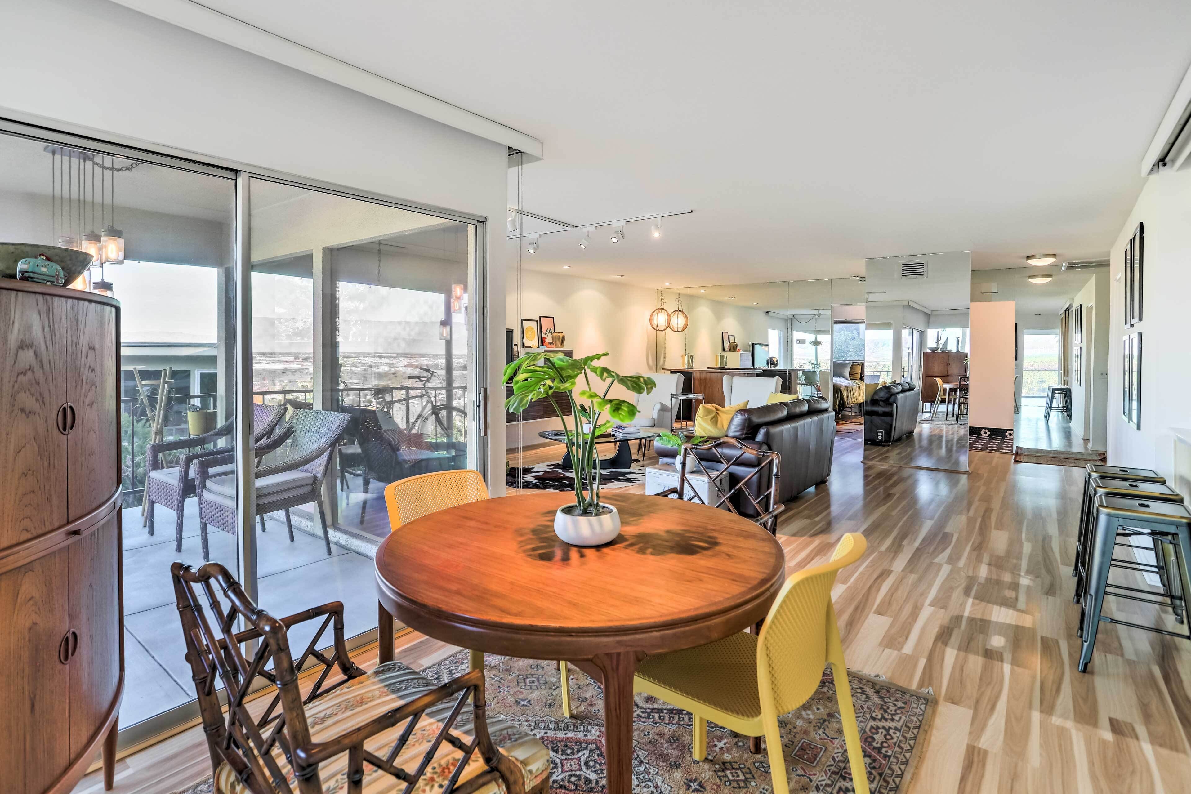 A modern living room with a wooden dining table, yellow chairs, and a large window.