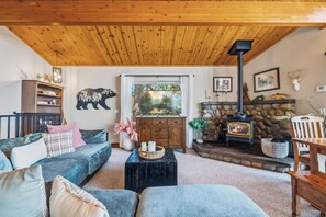 A cozy living room with a stone fireplace, a sofa, a coffee table, and a bookshelf. - Hot Tub + Scenic Views: Luxury Twain Harte Cabin! (Twain Harte)
