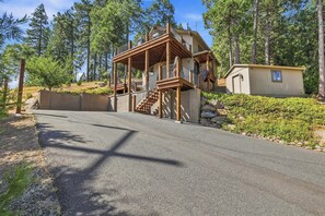 Eine zweistöckige Holzhütte mit einem Balkon, einer Steinmauer und einem kleinen Geräteschuppen.