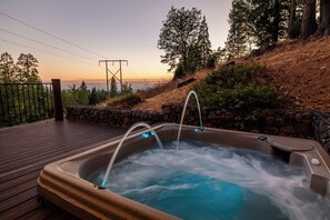 Ein Whirlpool auf einer Holzterrasse mit Blick auf einen Sonnenuntergang und Bäume.