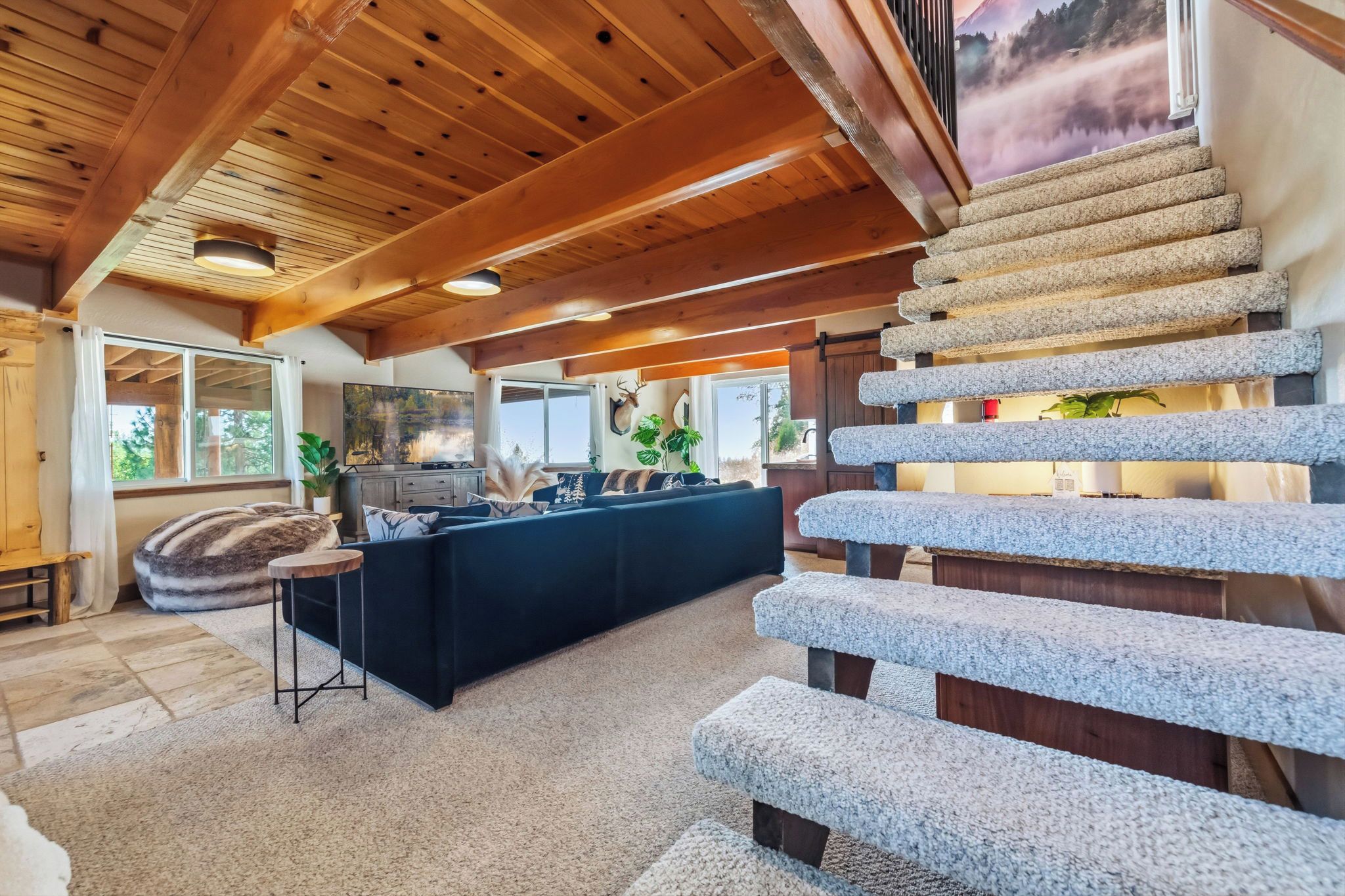 Un intérieur moderne avec un escalier en pierre, un canapé foncé et un téléviseur dans une pièce aux poutres apparentes.